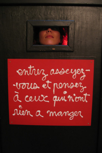 Dall'esterno la porta della cabina di legno. Su un pannello rosso attaccato alla porta sta scritto a caratteri bianchi l'invito ad entrare e pensare. Sulla finestrella si appoggia il mento di una donna.