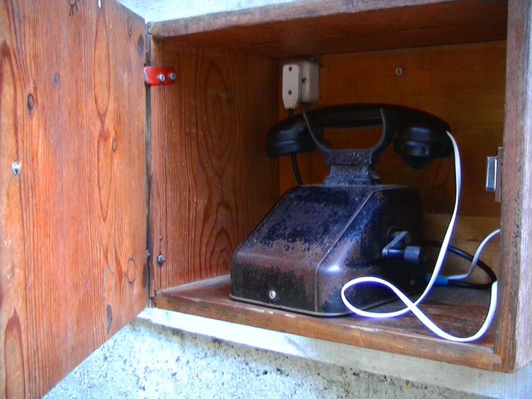 Un telefono a manovella chiuso in una armadietto di legno.