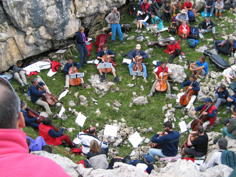 In una conca tra le rocce i violoncellisti formano un cerchio. In giro la gente si sistema come può.